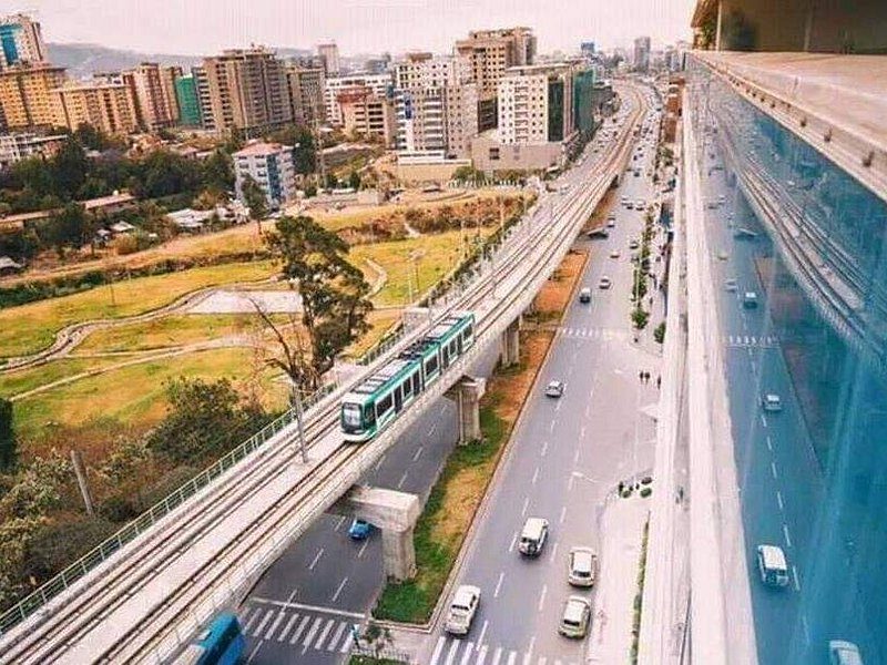 A green Addis Ababa Light Rail tram on its elevated viaduct beside a multi-lane ring road
